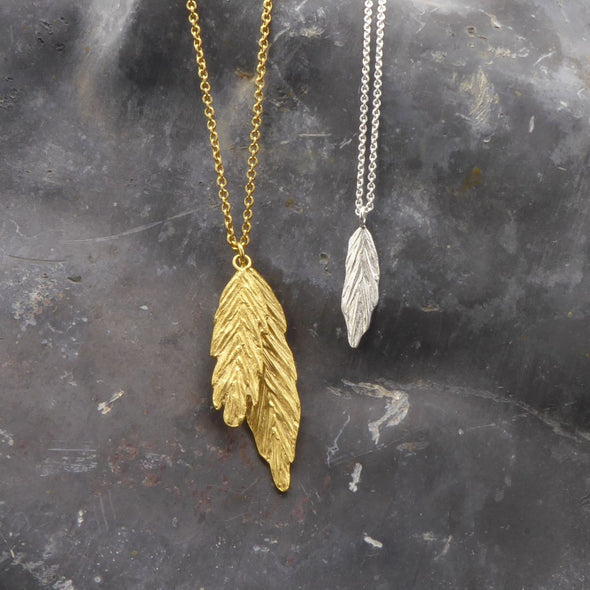 zwei-ketten-mit-feder-anhaengern-in-verschiednen-varianten-eine-kette-in-sterling-silber-mit-einem-kleinen-zarten-anhaenger-in-federform-die-andere-kette-in-vergoldetem-sterling-silber-hat-zwei-verschieden-grosse-federanhaenger-uebereinander-als-verschluss-der-ketten-in-vergoldetem-sterling-silber-ist-ein-karabiner-befestigt-den-man-auf-zwei-verschiedene-laengen-einhaken-kann-handgefertigt-in-unserer-goldschmiede-in-frankfurt-am-main