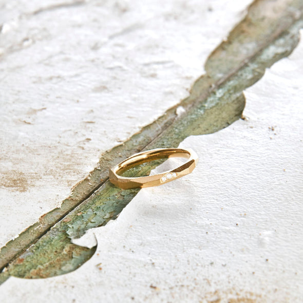 ein-ganz-schmaler-ring-mit-vielen-unregelmaessigen-facetten-beziehungsweise-polygonen-flaechen-der-ring-ist-ca-zweieinhalb-millimeter-breit-und-besteht-aus-gelbgold-er-ist-auch-in-fairtrade-gold-erhaeltlich-auf-einer-facette-sind-vollflaechig-drei-brillanten-eingefasst-ein-design-trauring-oder-verlobungsring-der-nicht-von-der-stange-ist-die-ringe-werden-von-hand-in-unserer-goldschmiede-in-frankfurt-am-main-angefertigt-alexandra-baum-schmuck