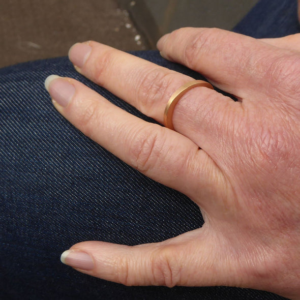am-finger-getragener-ehering-mit-dem-namen-durch-dick-und-duenn-der-ring-besteht-aus-rosegold-die-form-ist-klassisch-aber-leicht-unregelmaessig-an-manchen-stellen-dicker-an-manchen-stellen-duenner-ein-design-trauring-der-sich-von-der-masse-abhebt-die-ringe-werden-von-hand-in-unserer-goldschmiede-in-frankfurt-am-main-angefertigt