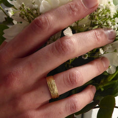 ein-grasring-sechs-millimeter-breit-aus-gelbgold-am-finger-getragen-im-hintergrund-ein-brautstrauss