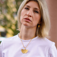 ein-blondes-model-traegt-gras-ohrhaenger-in-der-groesseren-variante-mit-einem-eirigen-anhaenger-mit-einer-struktur-von-echtem-gras-und-einen-grossen-ginkgo-anhaenger-zum-befestigen-im-ohr-haben-die-ohrringe-einen-buegel-der-mit-einem-silikonroehrchen-verschlossen-wird-die-schmuckstuecke-bestehen-aus-vergoldetem-recycling-sterling-silber-nachhaltiger-schmuck-von-hand-gefertigt-in-unserer-goldschmiede-in-frankfurt-bockenheim-alexandra-baum-schmuck